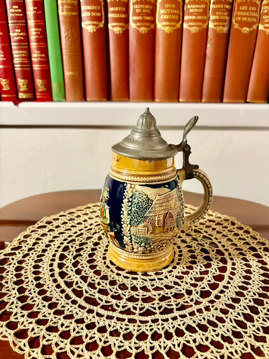 Decorative ceramic stein with lid on a lace doily in front of books