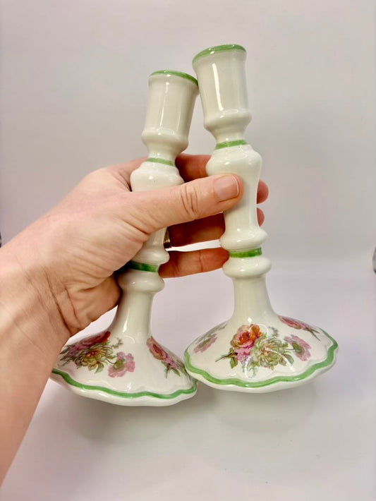 Hand holding two decorative ceramic candlesticks with floral designs on a plain background