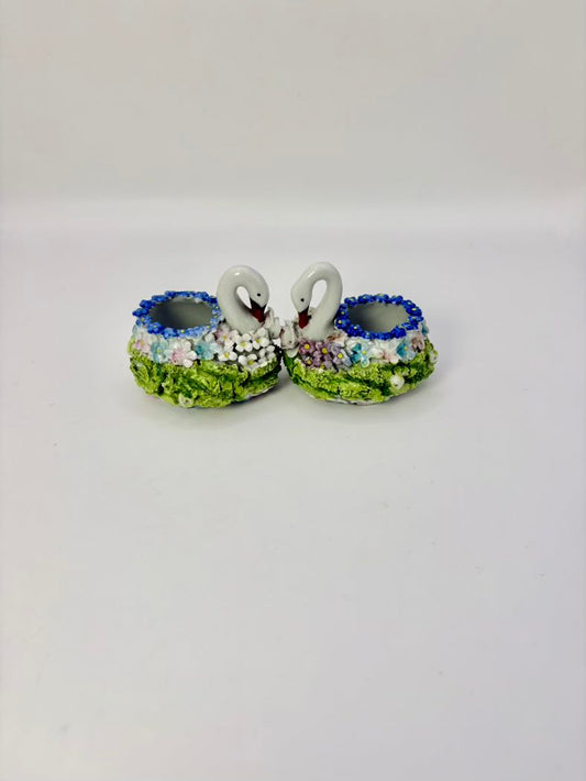 Two ceramic candle holders shaped like swans with blue bowls on a white background