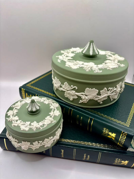 Two green ceramic jars with white floral patterns on a stack of books.