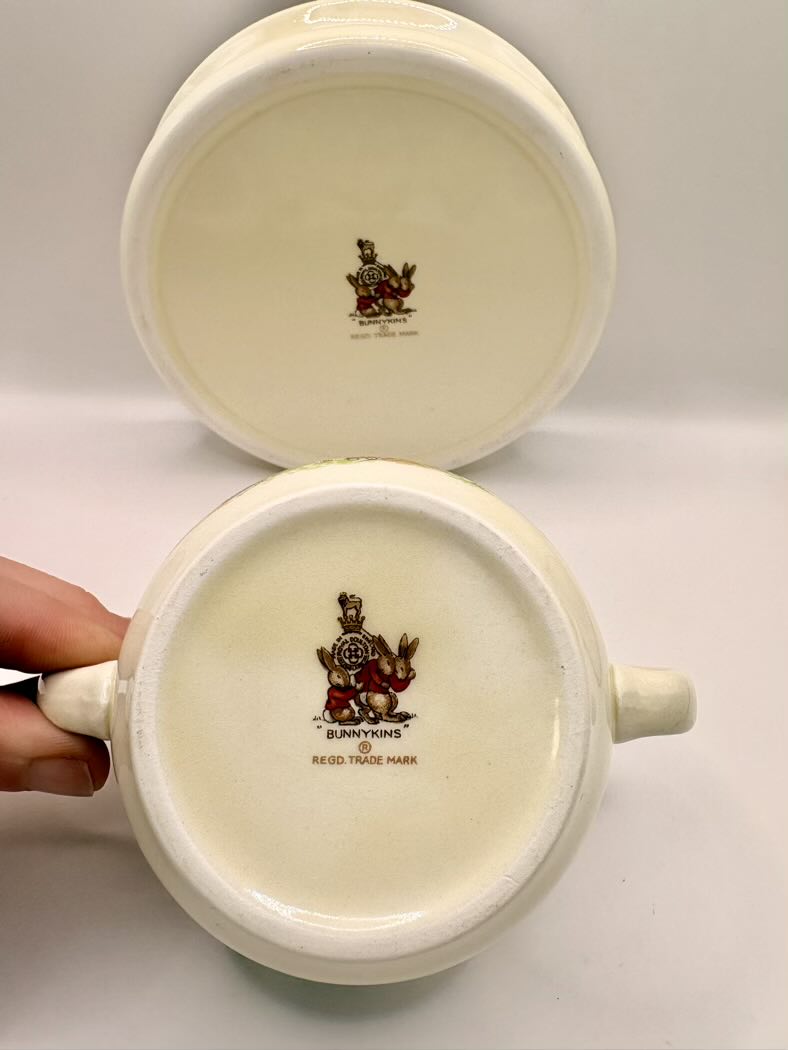 Two white ceramic pots with decorative logos on a light gray background