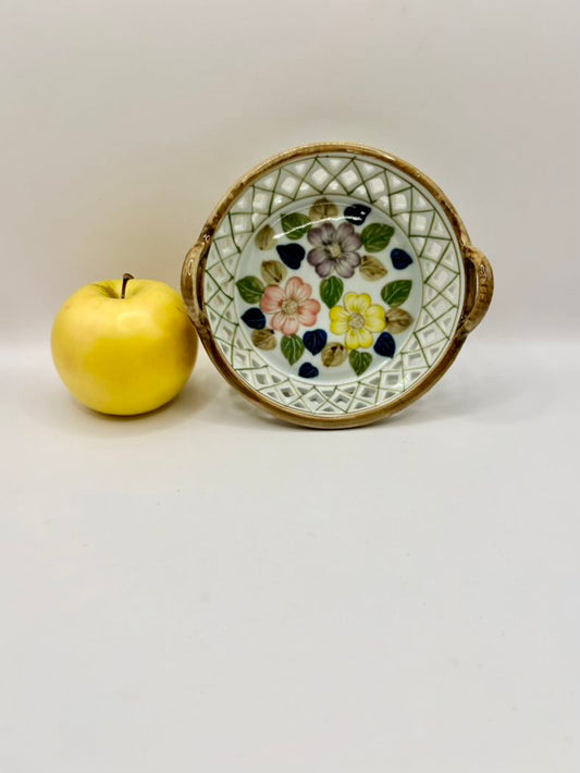 Decorative ceramic plate with floral design next to a yellow apple on a white background