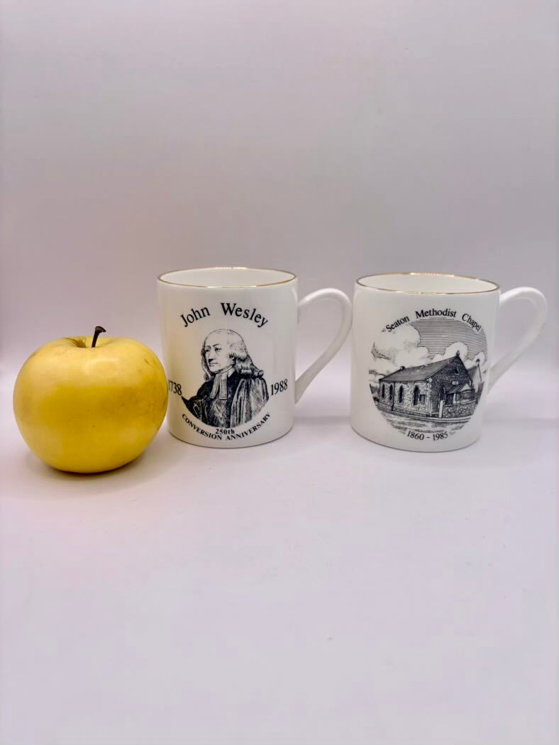 Two mugs with printed designs and a yellow apple on a white background