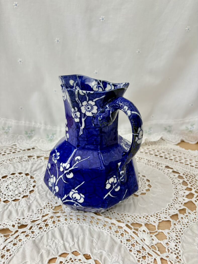 Blue ceramic pitcher with white floral patterns on a lace tablecloth