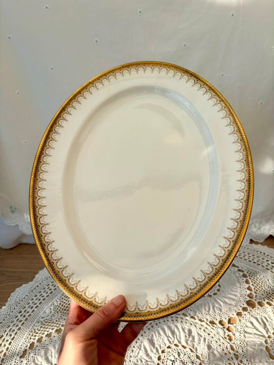 Decorative plate with gold rim held by a hand on a lace tablecloth.