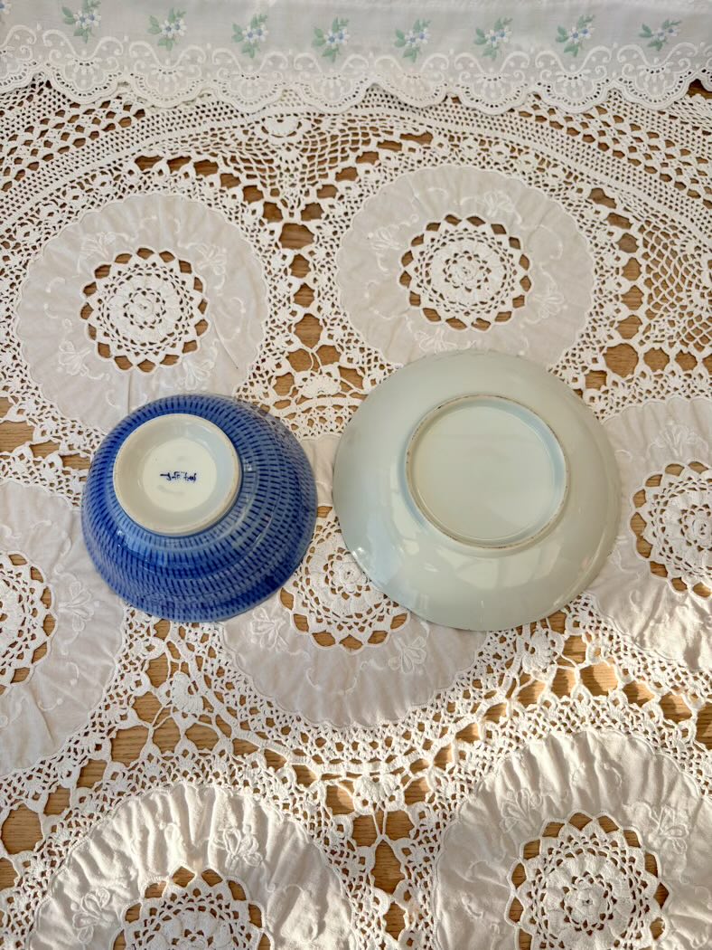 Two ceramic bowls, one blue and one white, on a lace tablecloth.
