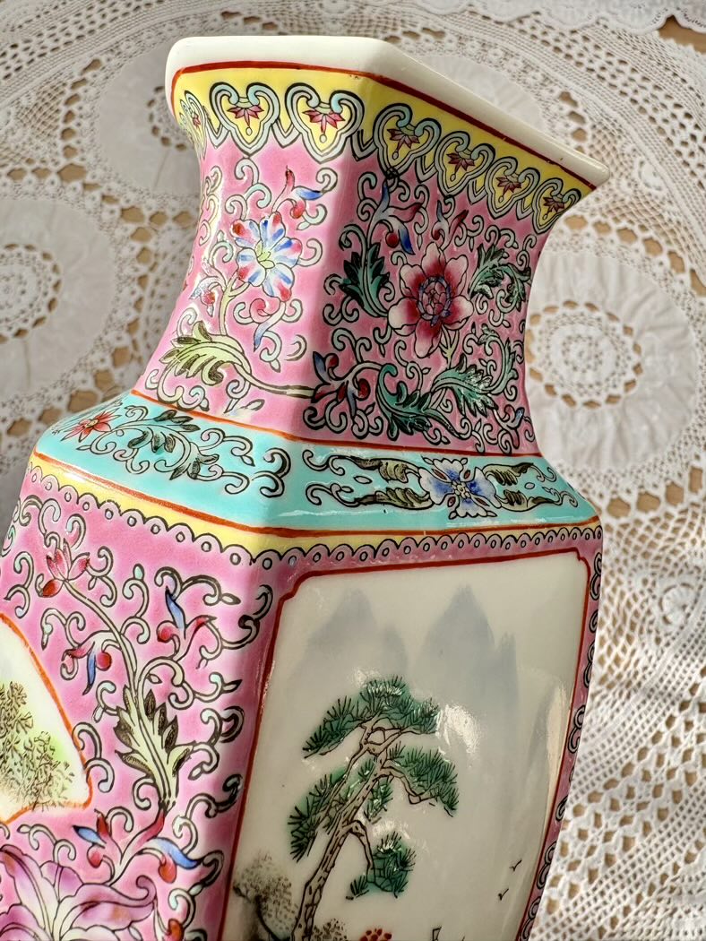 Colorful ceramic vase with floral and landscape designs on a lace tablecloth.