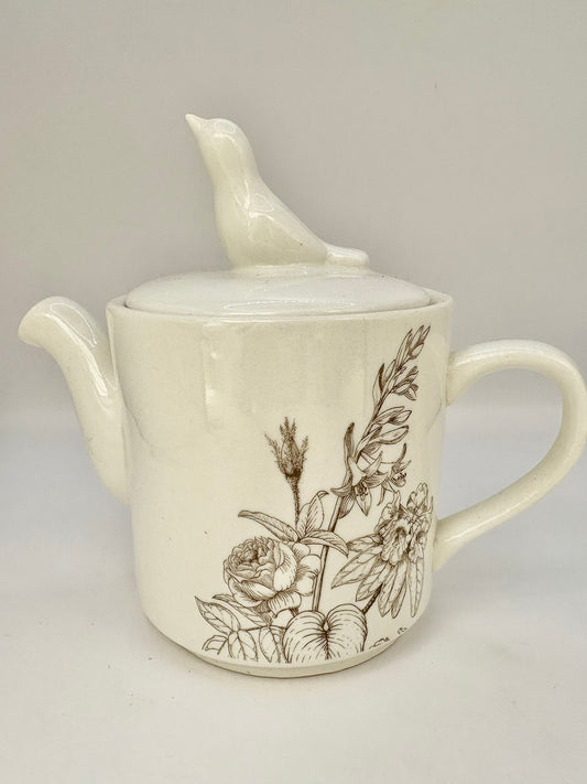 Ceramic teapot with floral design and bird on lid against a gray background
