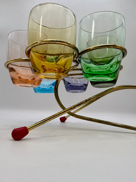 Set of colorful glass tumblers on a brass stand with a white background