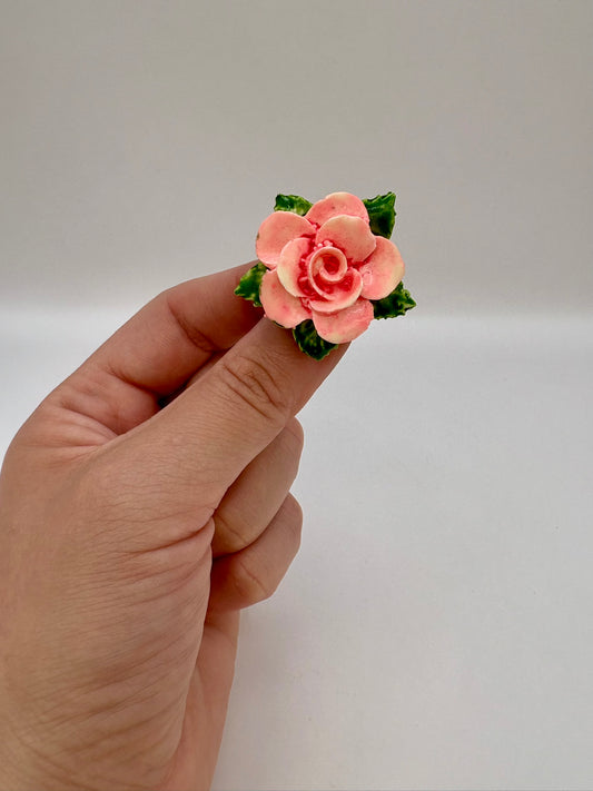 Hand holding a small pink rose flower against a plain background