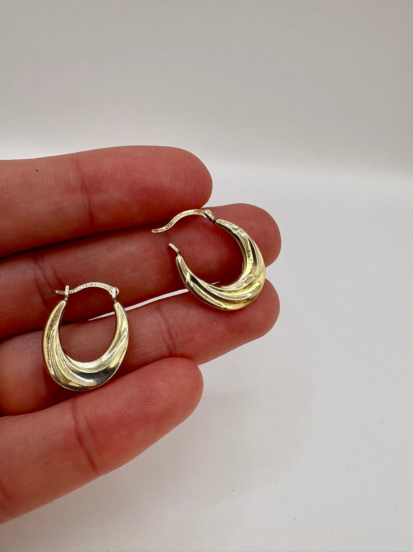 Gold hoop earrings held between fingers against a plain background