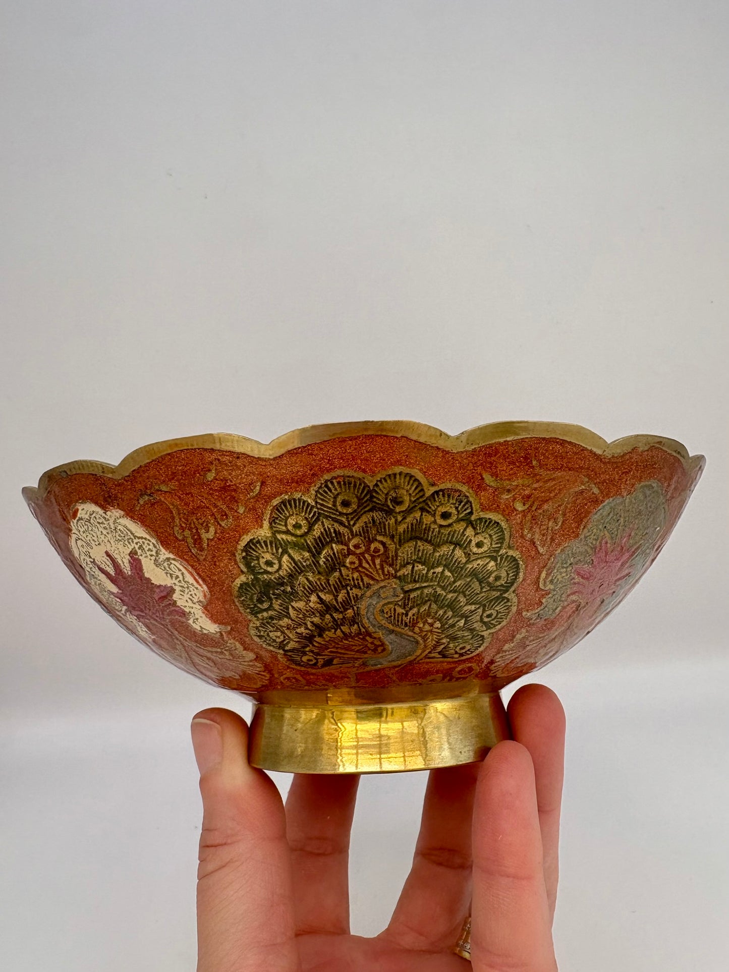 Decorative bowl with intricate designs held by a hand against a plain background