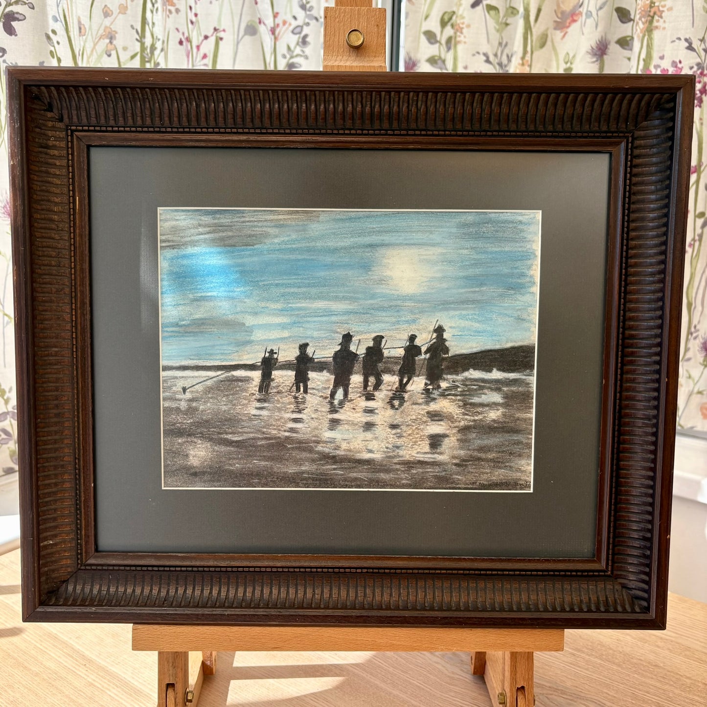 Framed artwork of people on a beach with a brown frame.
