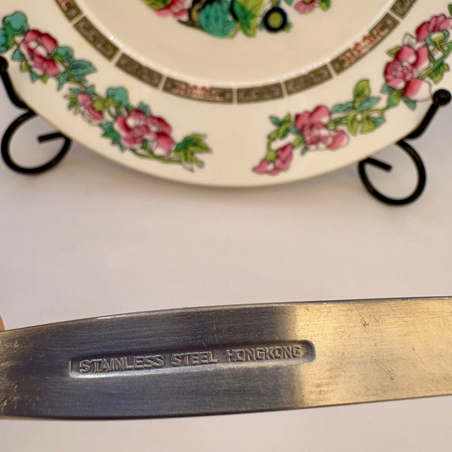 Metallic object with 'Stainless Steel Hong Kong' engraving in front of a floral-patterned plate.