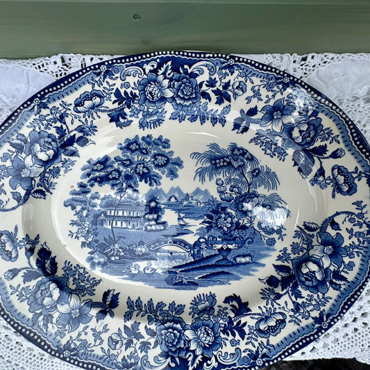 Decorative blue and white platter with floral and landscape design on a lace tablecloth.