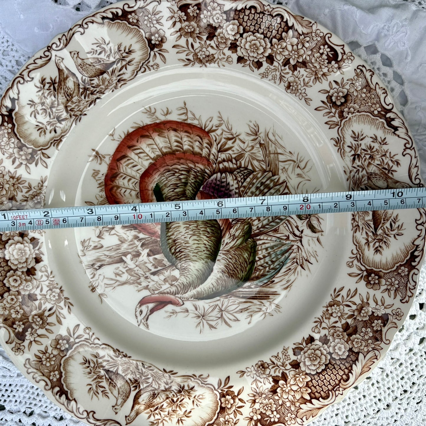 Decorative plate with a turkey design and floral patterns, measured against a ruler.
