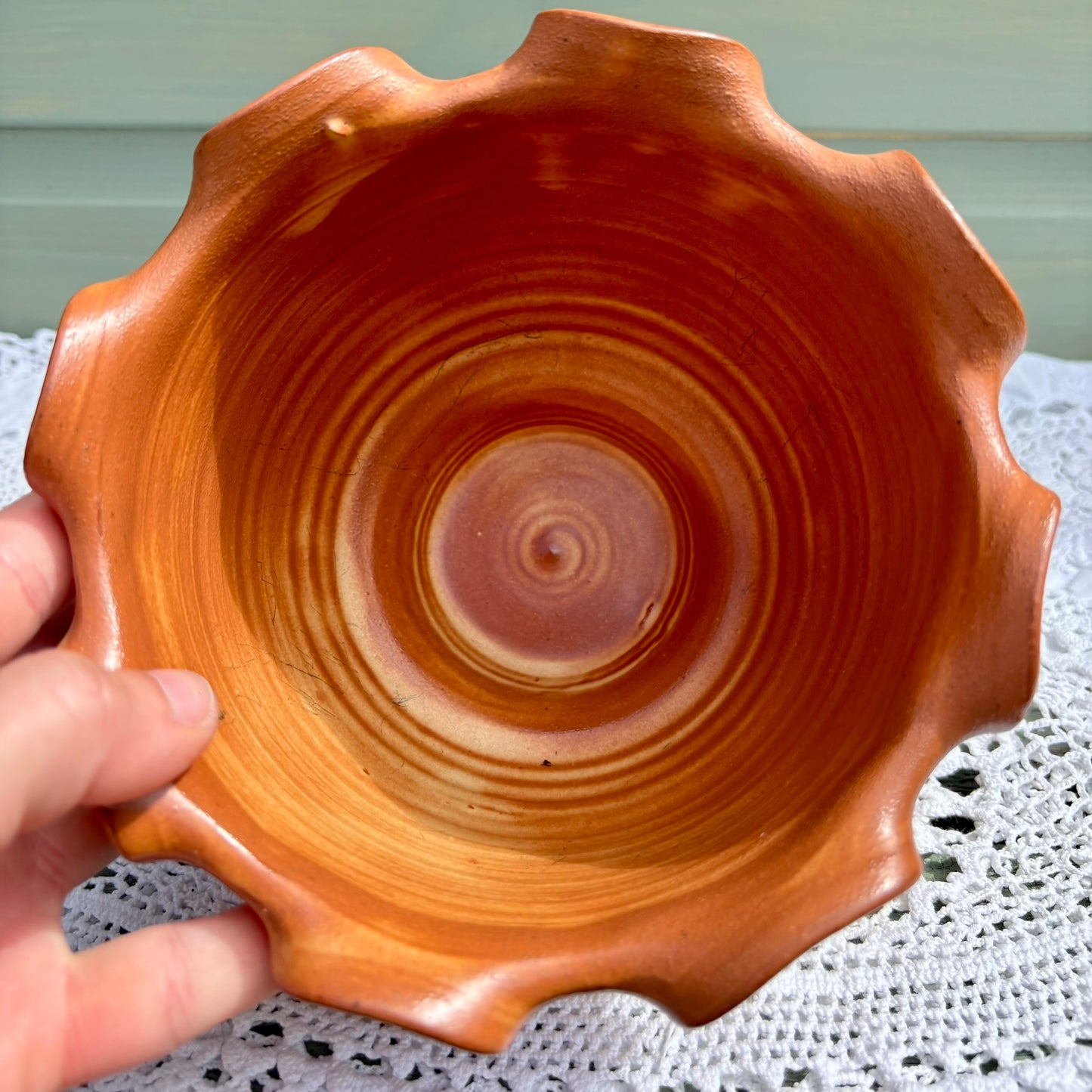 Hand holding a wooden bowl with concentric circular patterns on a white lace tablecloth.