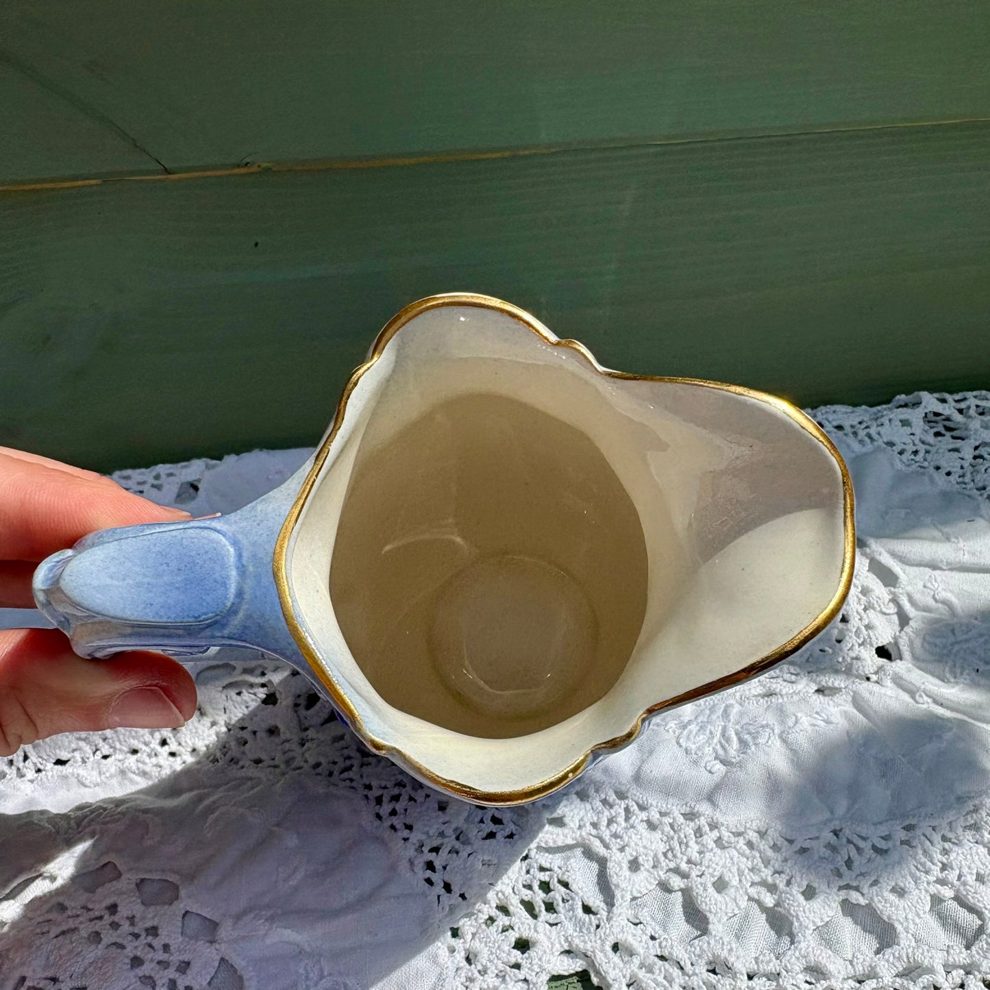 Decorative ceramic bowl with gold rim held by a hand on a lace tablecloth.