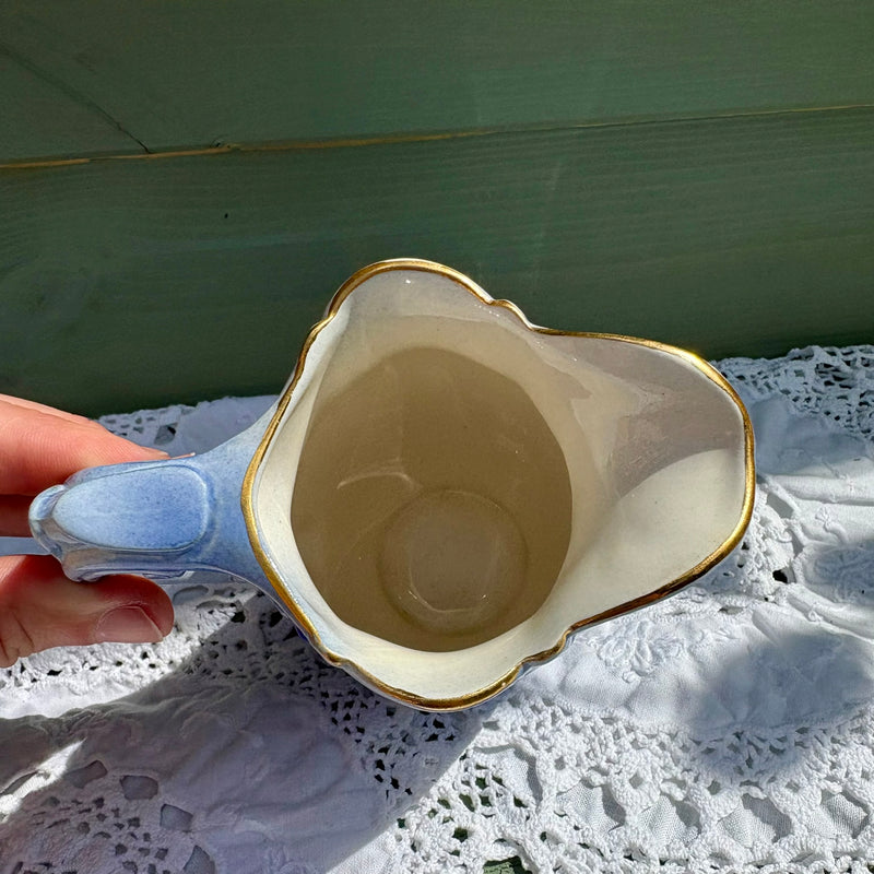 Decorative ceramic bowl with gold rim held by a hand on a lace tablecloth.