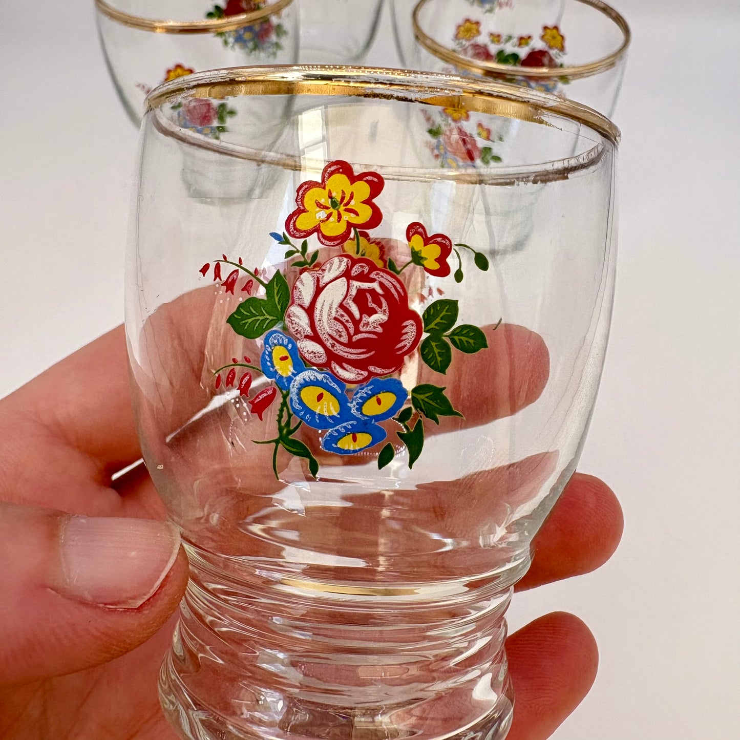 Clear glass with floral design held by a hand against a white background