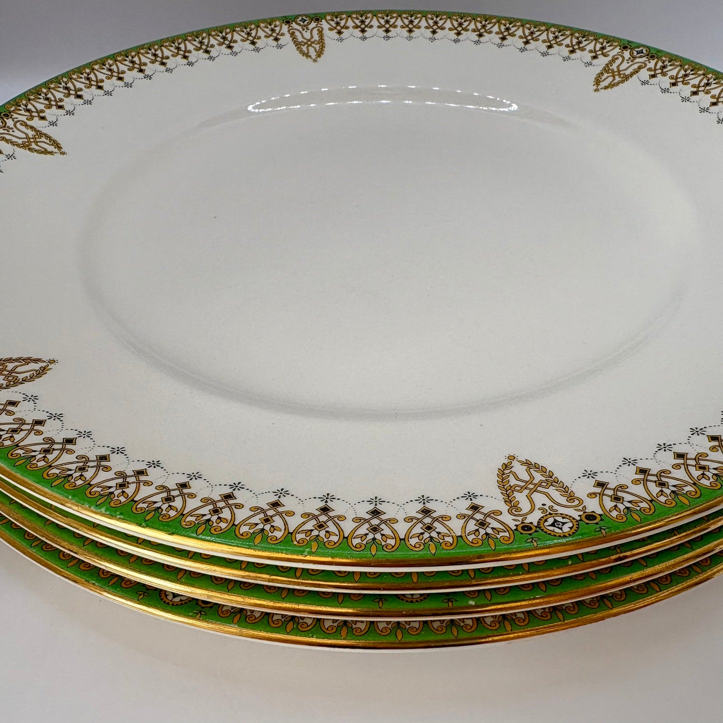 Set of four ornate plates with gold and green decorative rims on a white background