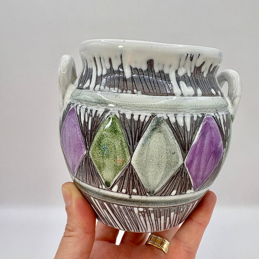 Ceramic vase with geometric design held by a hand against a plain background
