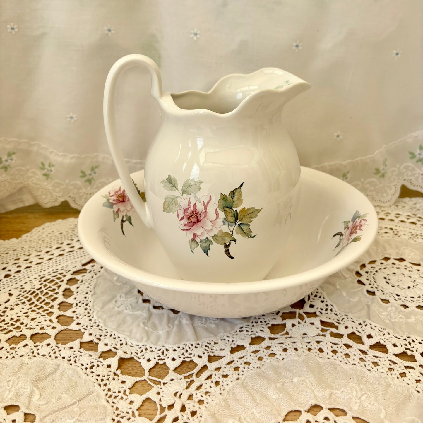 White ceramic pitcher with floral design on a matching saucer on a lace tablecloth.