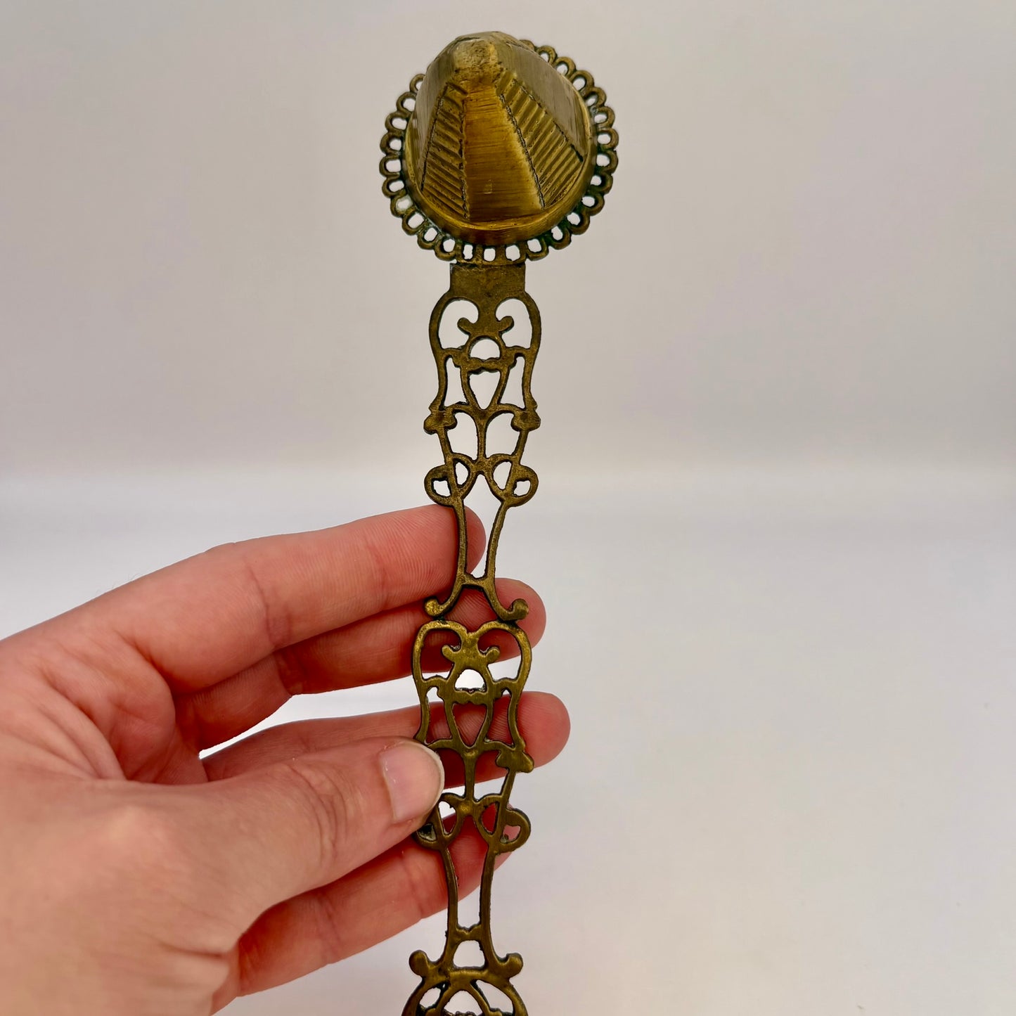 Hand holding a decorative brass spoon against a white background