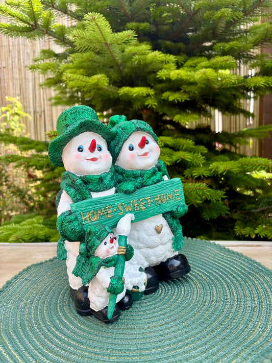 Two snowmen in green hats and scarves holding a 'Home Sweet Home' sign in front of a Christmas tree.