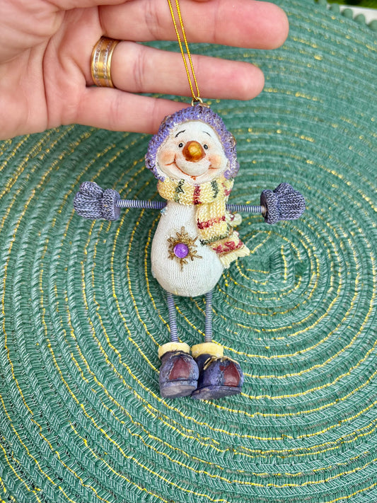 Decorative snowman ornament held by a hand on a textured green surface