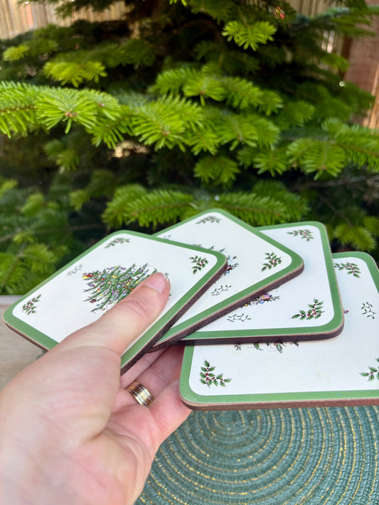 Hand holding a set of Christmas-themed coasters with a greenery background
