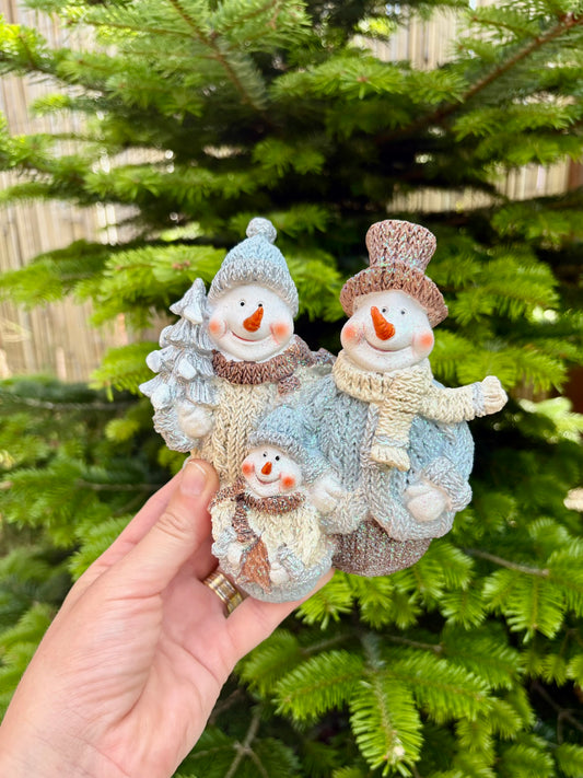 Decorative snowman ornament held in front of a Christmas tree