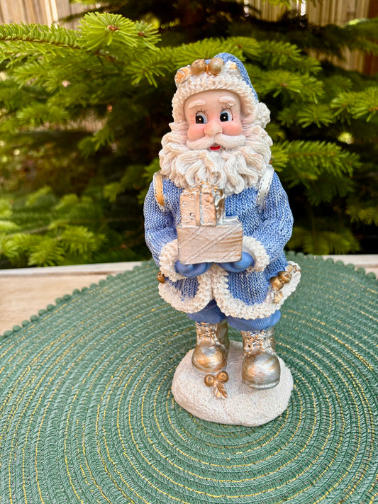 Decorative Santa figurine holding a gift box in front of a Christmas tree.