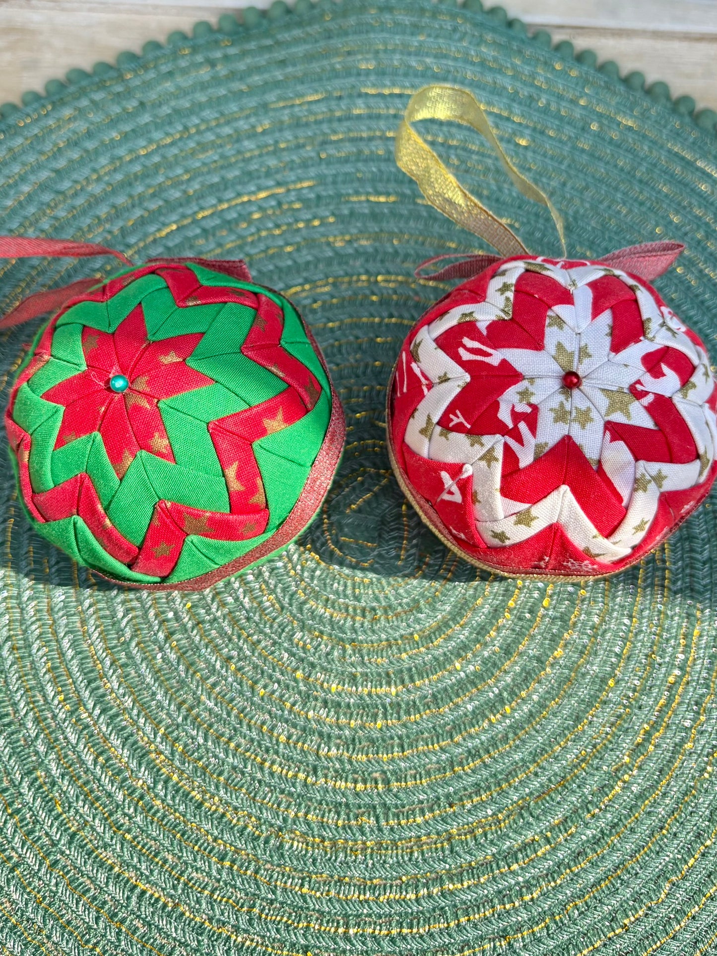 Two decorative Christmas balls with floral patterns on a textured green surface.