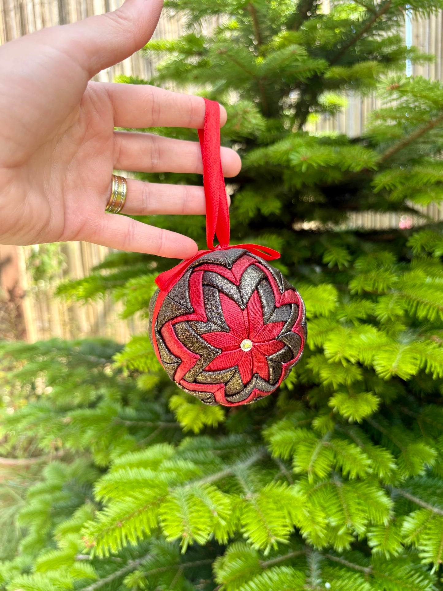 Decorative ornament with red and black pattern held in front of a Christmas tree.