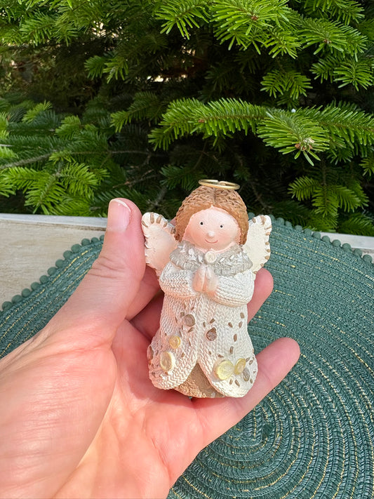Hand holding a decorative angel figurine in front of a Christmas tree.