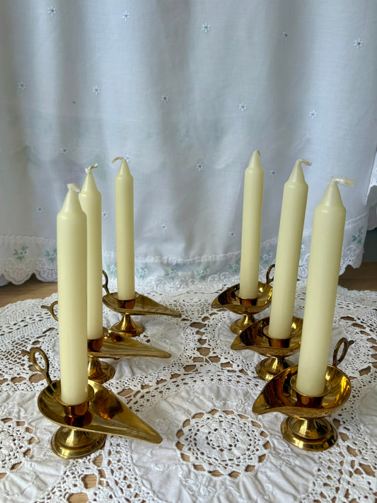 Set of four brass candle holders with white candles on a lace tablecloth.