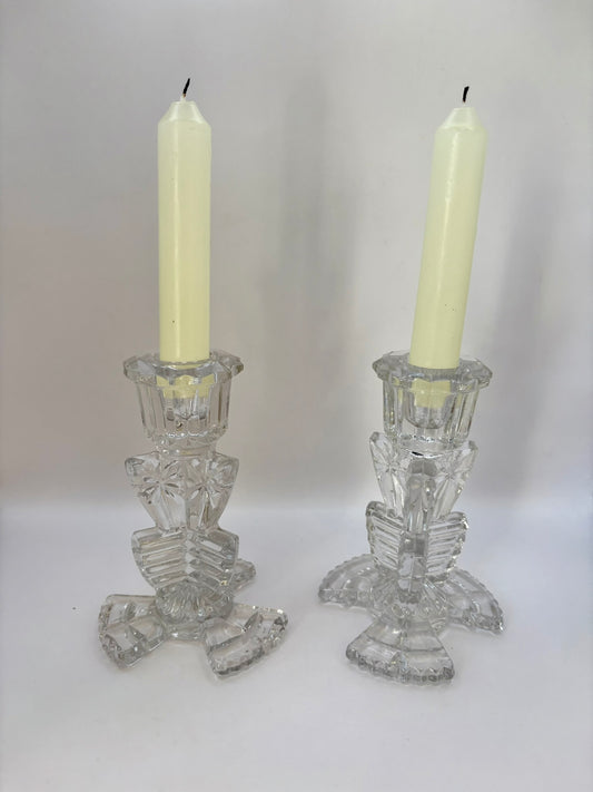 Two crystal candle holders with white candles on a plain background