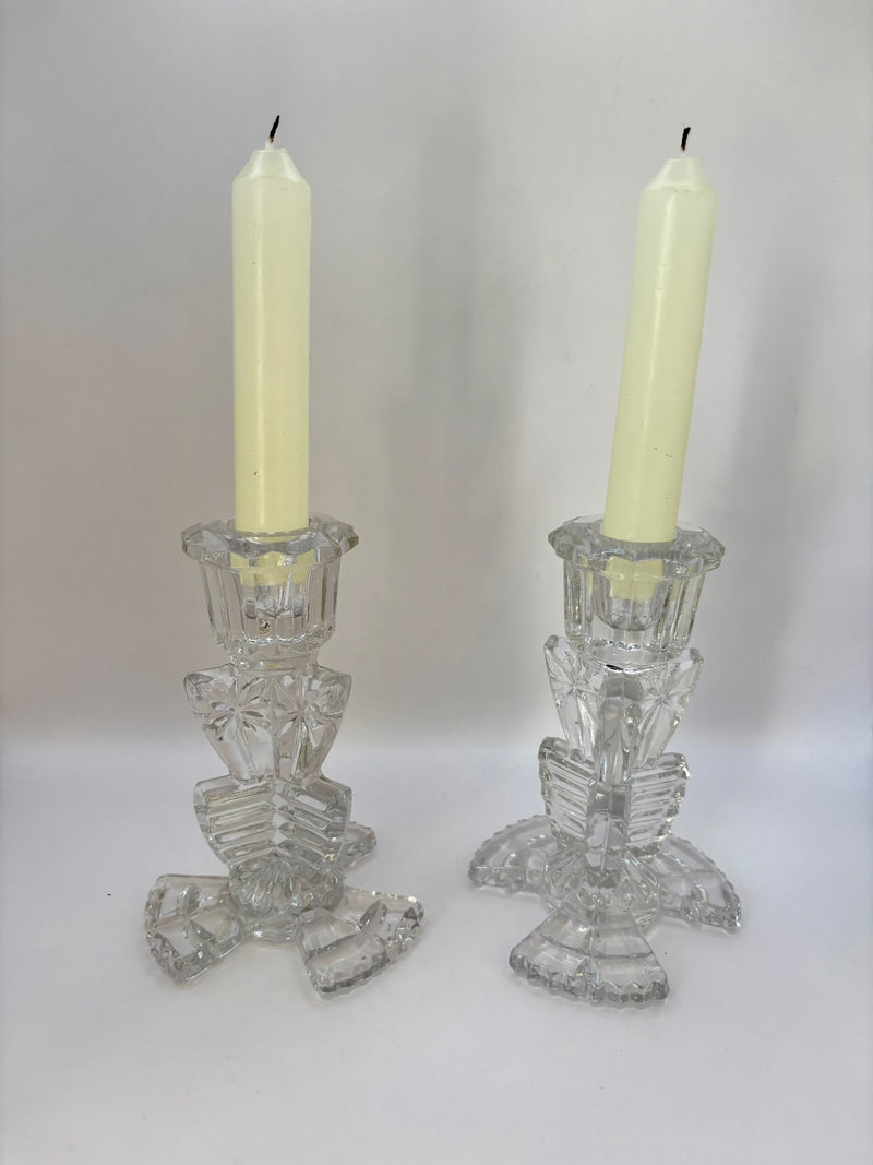 Two crystal candle holders with white candles on a plain background