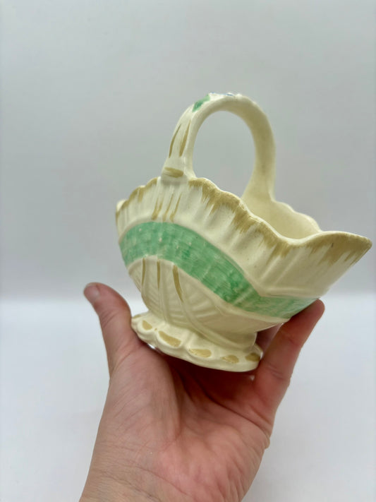Hand holding a ceramic basket with green interior against a white background