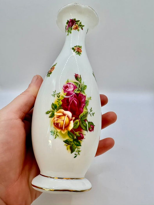 Decorative vase with floral design held by a hand against a plain background
