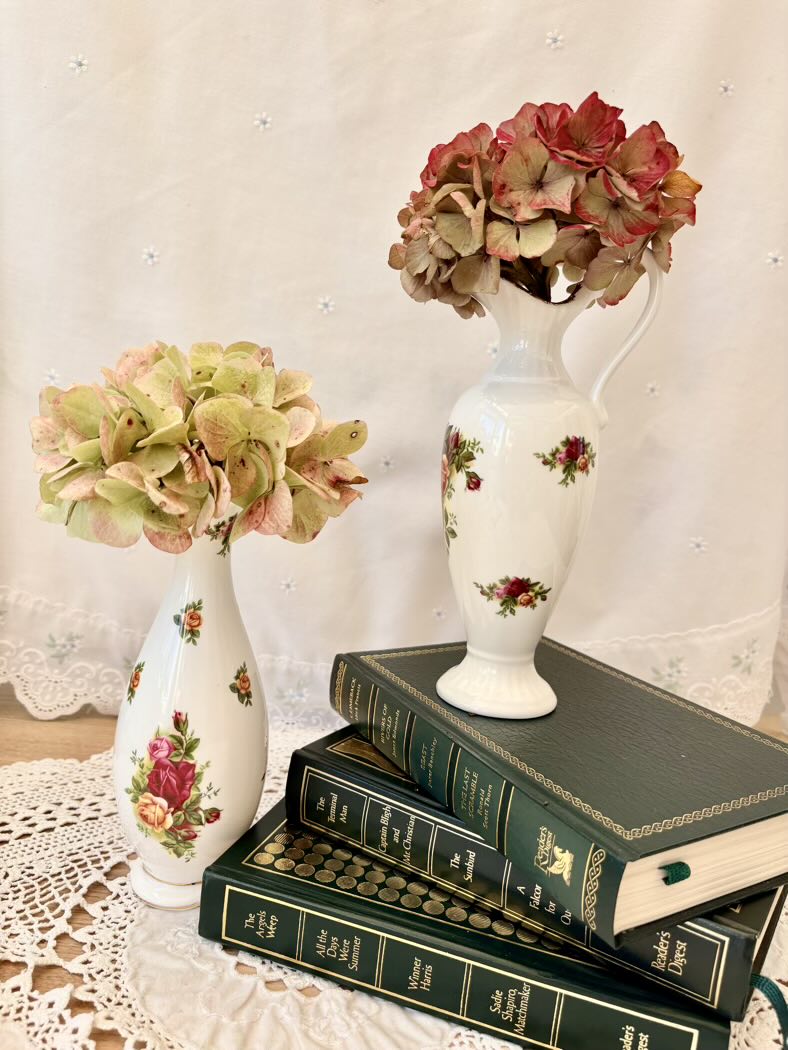 Decorative setup with floral vases and books on a lace tablecloth.