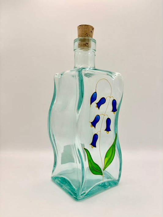 Decorative glass bottle with painted blue flowers and a cork on a white background