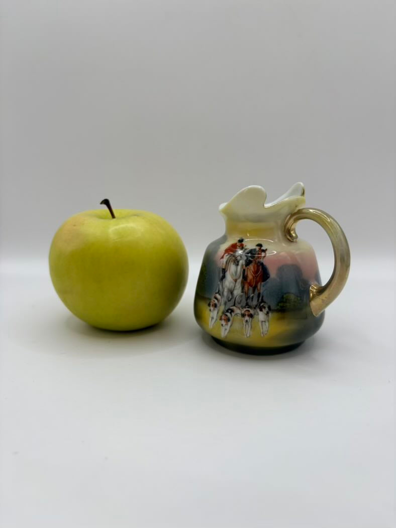 Green apple next to a ceramic pitcher with a decorative handle on a white background