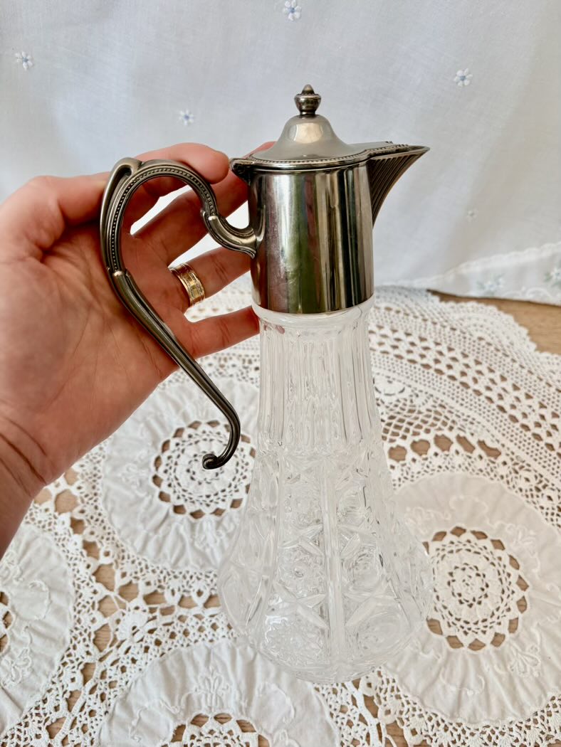 Hand holding a silver jug over a lace tablecloth