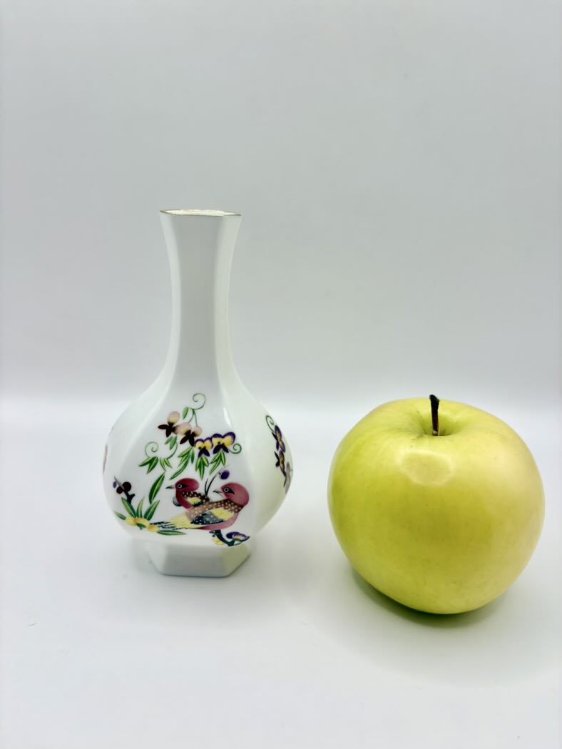Decorative vase with floral patterns next to a green apple on a white background