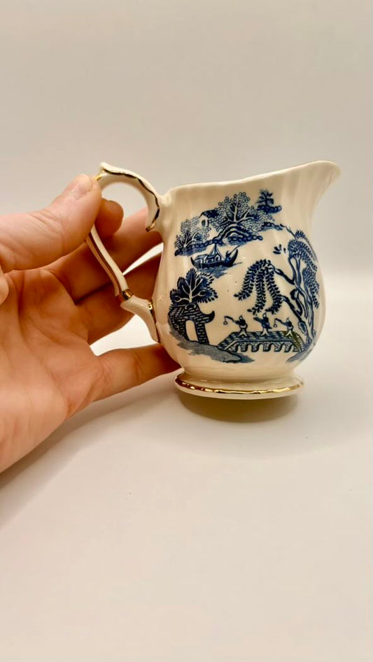 Hand holding a small white ceramic pitcher with blue floral patterns on a plain background