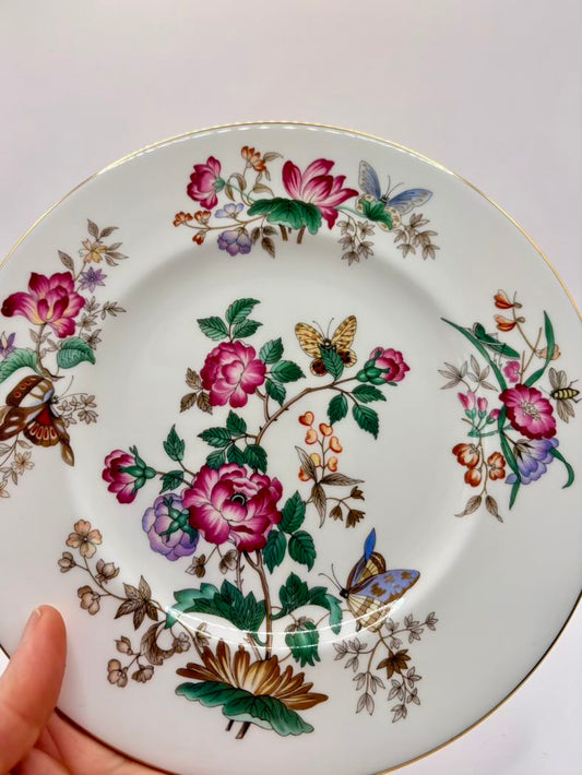 Decorative plate with floral and butterfly design held by a hand on a white background