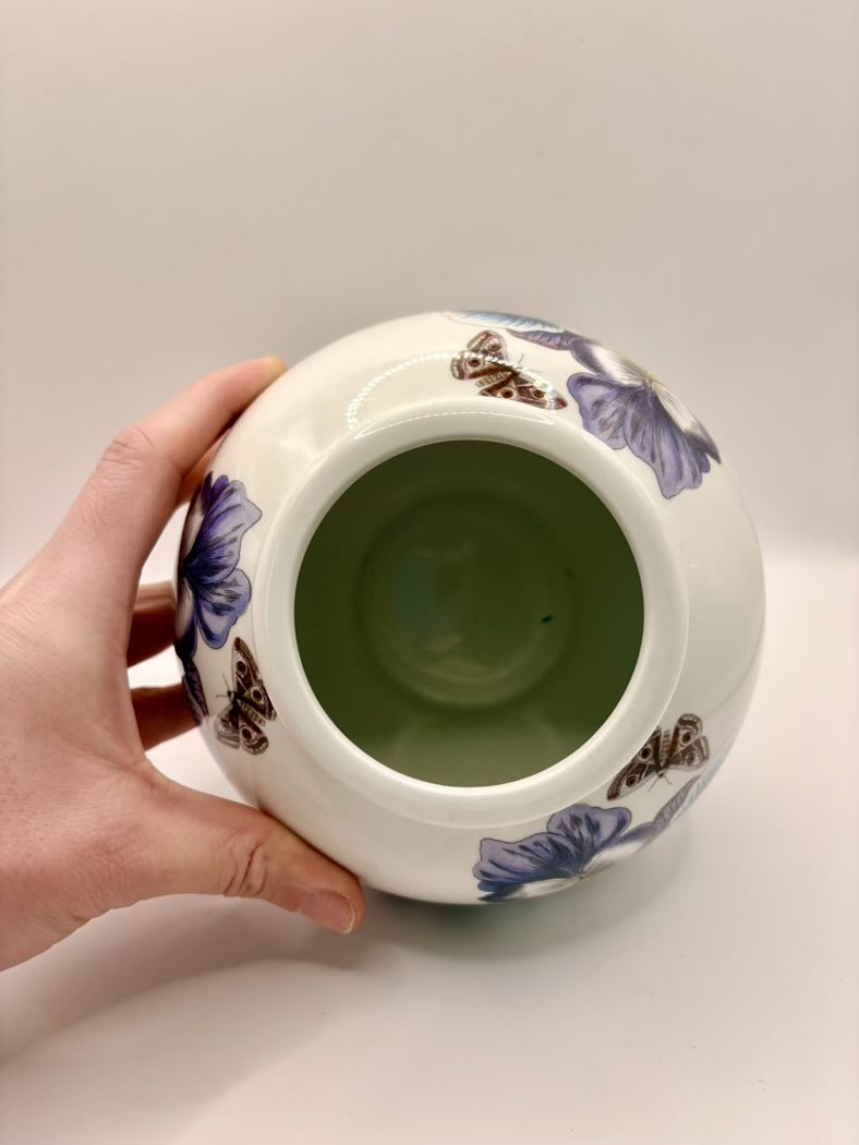 Ceramic jar with butterfly design held by a hand on a white background