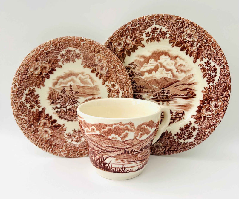 Ceramic mug and plates with brown scenic pattern on a white background
